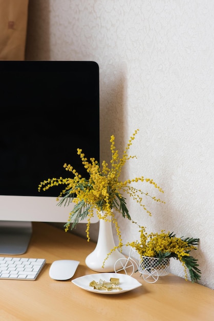 Bouquet di fiori di mimosa gialla in un vaso su un desktop con un computer