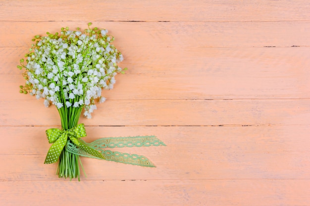 Bouquet di fiori di mughetto con fiocco e nastro su uno sfondo rosa in legno con uno spazio di copia