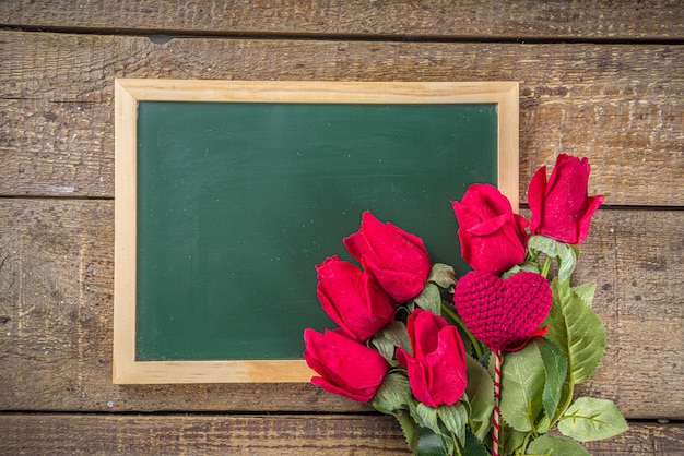 Bouquet di fiori di rosa rossa con cuore rosso sulla tavola di legno con una lavagna. Vacanze di San Valentino