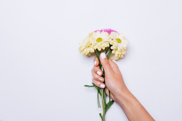 Bouquet di fiori gialli e viola in mano femminile con manicure bianca