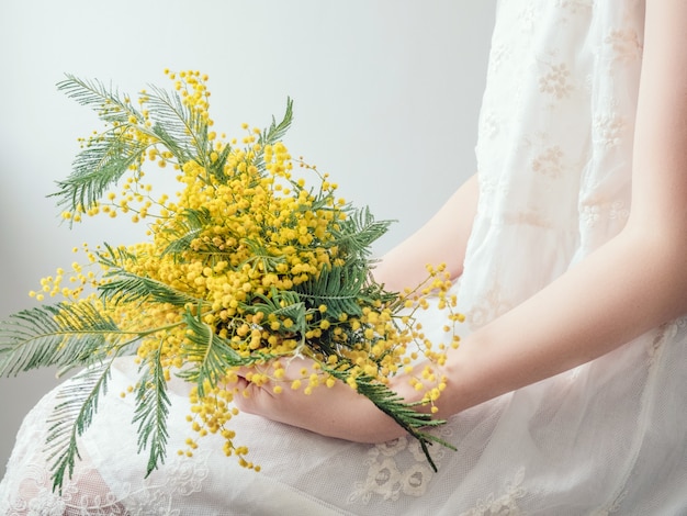 Bouquet di fiori gialli luminosi nelle mani di una giovane donna in abito bianco