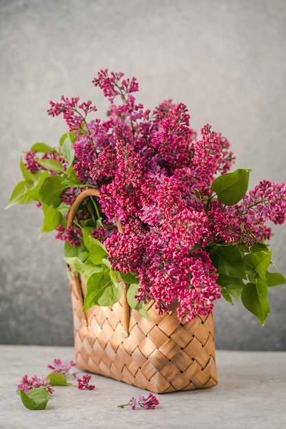 Bouquet di fiori lilla colorati in un cesto di vimini su sfondo di cemento concrete