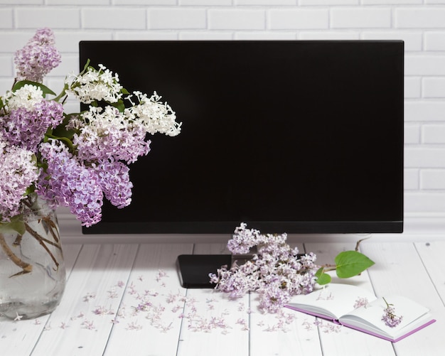 Bouquet di fiori lilla schermo monitor nero mattone bianco sfondo in legno prospettiva vista frontale