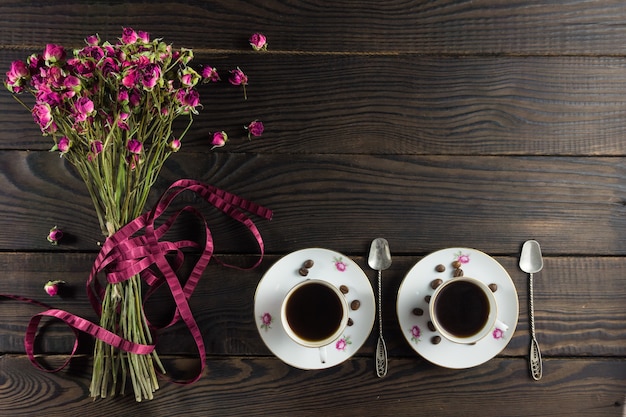 Bouquet di fiori secchi con un nastro sulla superficie in legno scuro. Due tazzine da caffè e due piattini in porcellana