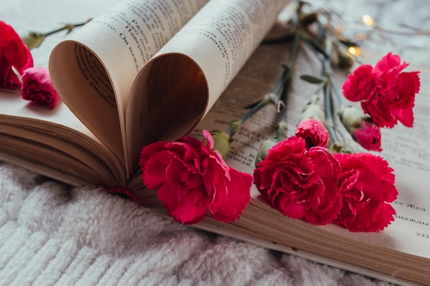 Bouquet di garofani in miniatura rosa che si trovano sulle pagine di un libro su un maglione bianco lavorato a maglia
