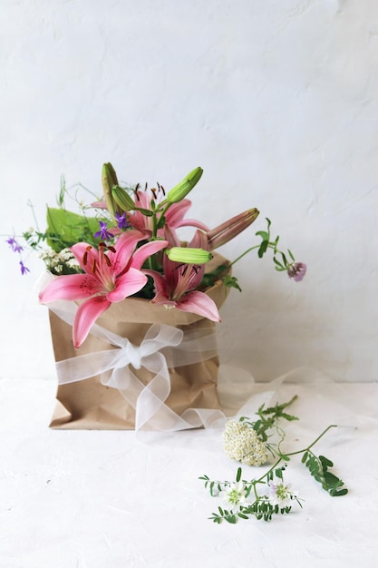 Bouquet di gigli rosa freschi un pacchetto con fiori su uno sfondo chiaro congratulazioni romantiche