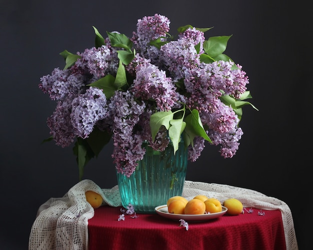 Bouquet di lillà viola in un vaso blu e albicocche sul piatto o