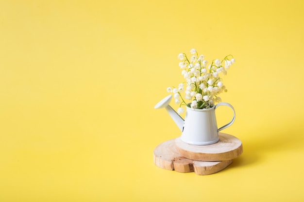 Bouquet di mughetti in un annaffiatoio decorativo su sfondo giallo con spazio per la copia