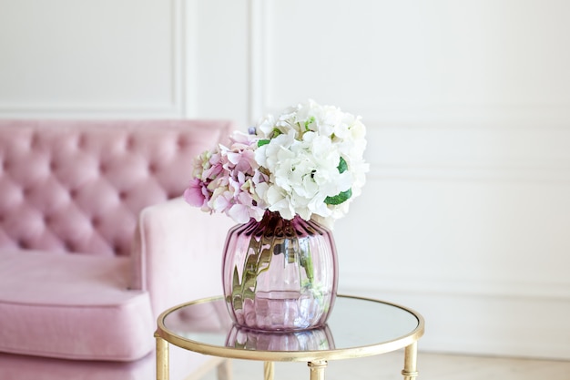 Bouquet di ortensie pastello in vaso di vetro. Fiori in un vaso a casa. bellissimo bouquet di ortensie è in un vaso su un tavolo vicino a un divano rosa in un salotto bianco. Arredamento d'interni per la casa. Scandinavia