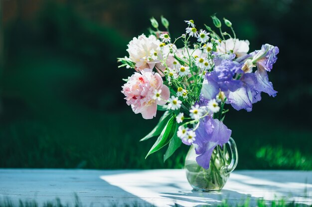 Bouquet di peonie bianche, camomille e fiori di iris in vaso di vetro. Sfondo estivo. Foto colorata.