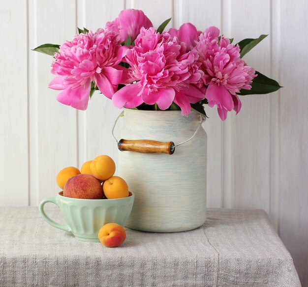 Bouquet di peonie rosa, pesche e albicocche in tavola.