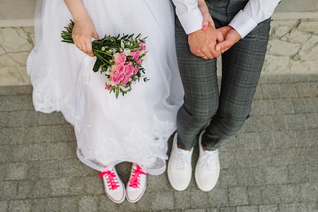 Bouquet di rose bianche e rosa nelle mani della sposa Gli sposi si tengono per mano e indossano scarpe da ginnastica rosa Divertenti sposi Gli sposi insieme Primo piano Vista dall'alto