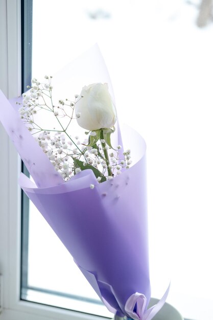 Bouquet di rose bianche in confezione viola sul davanzale della finestra