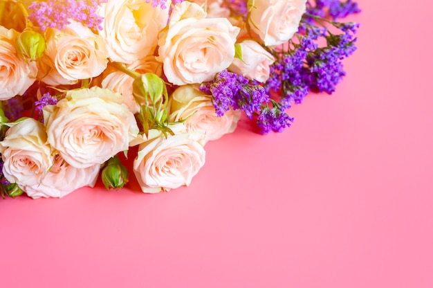 bouquet di rose crema e fiori viola brillante in piena fioritura su uno sfondo rosa con spazio per il testo.