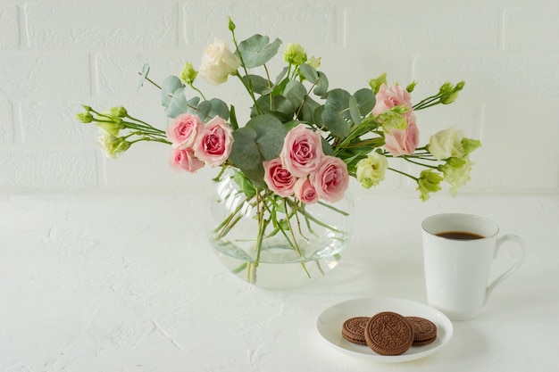 Bouquet di rose, eustoma ed eucalipto in un elegante vaso di vetro su un tavolo. Composizione di fiori per la decorazione d'interni.