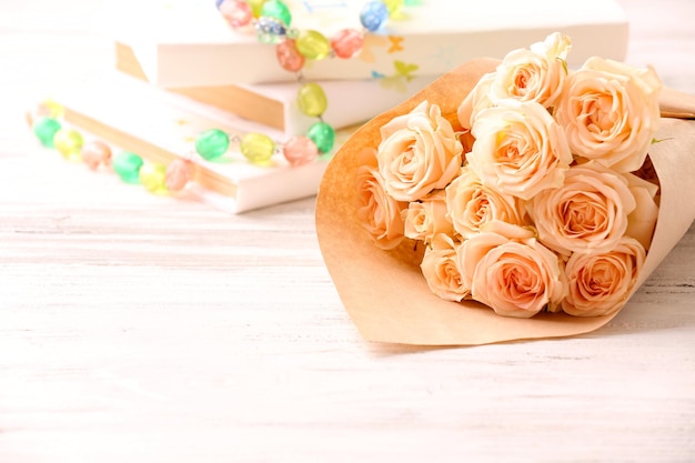 Bouquet di rose fresche avvolte in carta con libri e perline su sfondo di legno