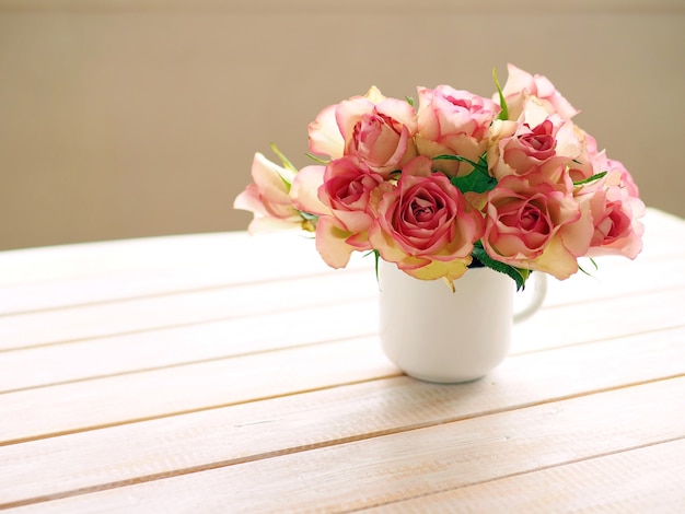 Bouquet di rose rosa in tazza bianca sul tavolo di legno