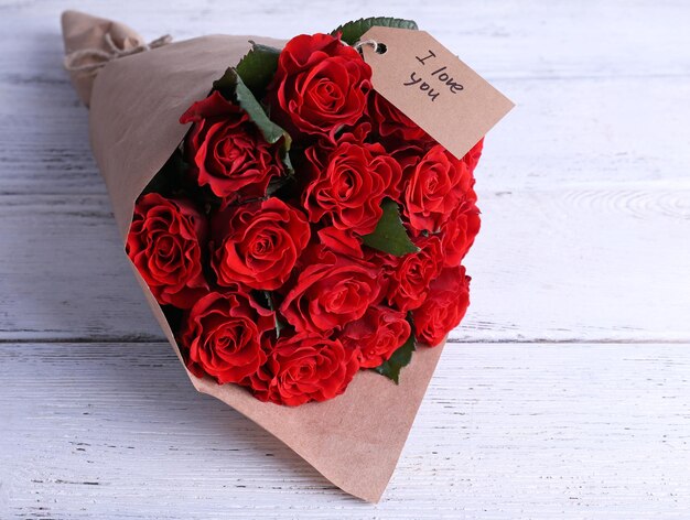 Bouquet di rose rosse con cartellino avvolto in carta su fondo in legno