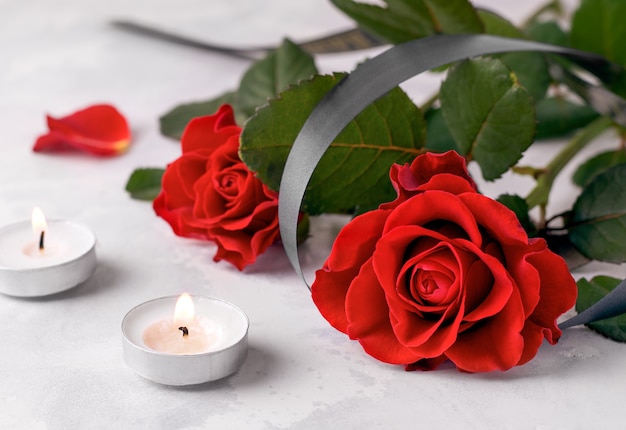 Bouquet di rose rosse fresche accanto a due candele in lutto