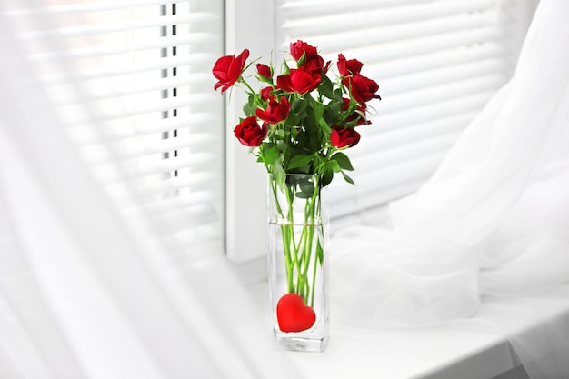 Bouquet di rose rosse in vaso di vetro con cuore su sfondo davanzale