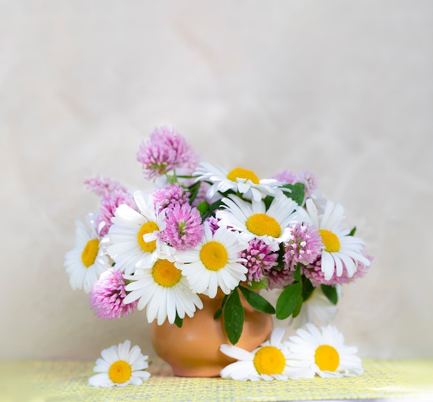 Bouquet di trifoglio e camomilla in un vaso su sfondo chiaro. Bouquet estivo di fiori da giardino e di campo. Natura morta con margherite. messa a fuoco selettiva