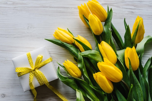 Bouquet di tulipani con confezione regalo su sfondo di legno bianco Spazio per il messaggio Concetto di fiori Biglietto di auguri per le vacanze per San Valentino Festa della mamma delle donne Pasqua Compleanno Vista dall'alto laici piatta