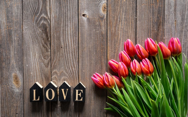 Bouquet di tulipani e parola decorativa Amore su uno sfondo di legno piatto vista superiore