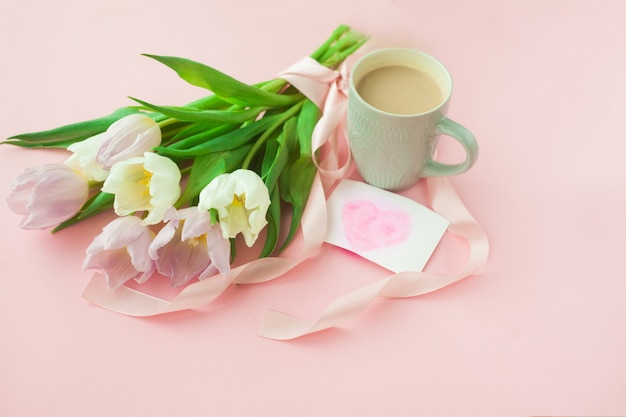 Bouquet di tulipani e una tazza di caffè su uno sfondo rosa pastello.