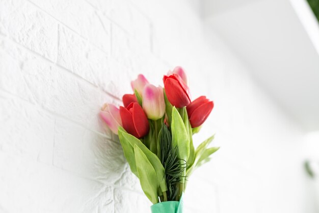 Bouquet di tulipani primaverili con fiori di colore diverso avvolti in carta per regalo su sfondo bianco.