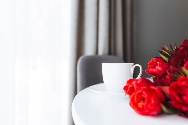 Bouquet di tulipani rossi sul tavolo e tazza di caffè bianco