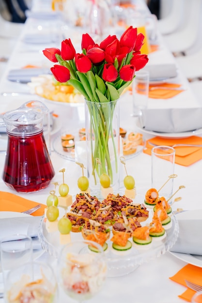 bouquet di tulipani rossi sulla tavola festiva. servire la tavola con antipasti, tartine, insalate in vasetto.