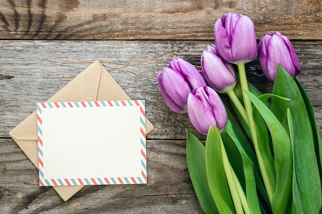 Bouquet di tulipani viola e biglietto di auguri in bianco su uno sfondo di legno vista superiore spazio di copia