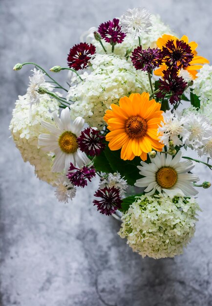 Bouquet di vari fiori estivi di ortensie margherite fiordalisi su sfondo grigio vista dall'alto Copia spazio