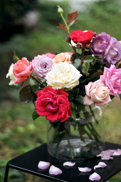 Bouquet floreale di diverse rose colorate in un vaso di vetro su un tavolo scuro con petali caduti.