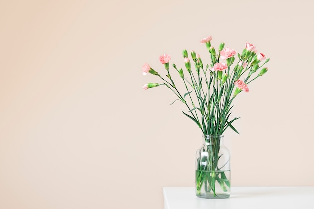 Bouquet fresco di fiori di garofano in un vaso di vetro sul tavolo bianco su sfondo beige chiaro con spa...