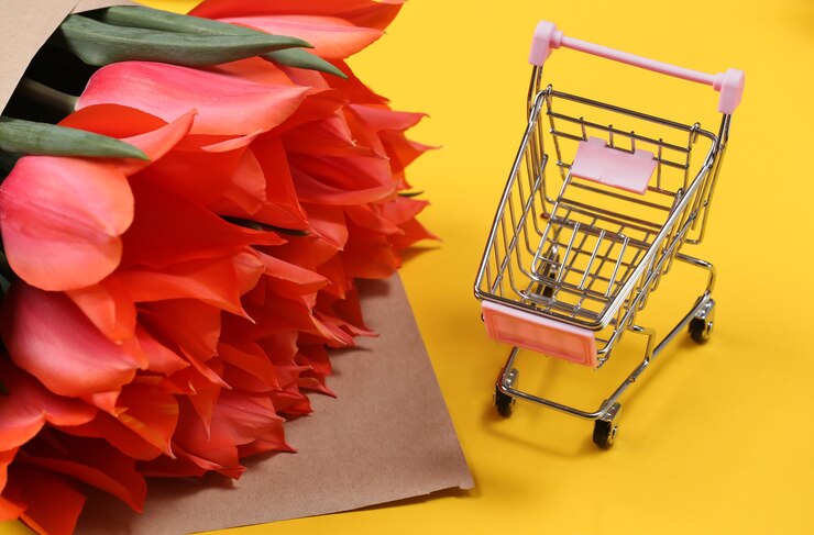 Bouquet of red tulips and supermarket trolley on yellow background.