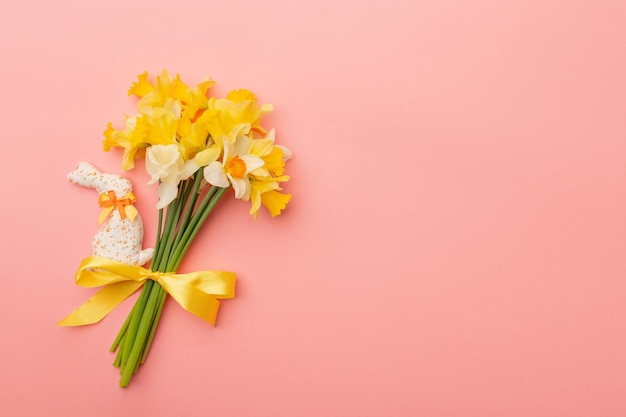 Bouquet primaverile giallo chiaro e coniglietto pasquale su sfondo rosa Sfondo di fiori primaverili con spazio per la copia