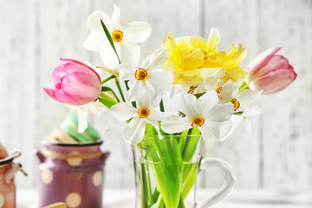 Bouquet primaverile in tazza di vetro e gustosi amaretti su sfondo di legno colorato