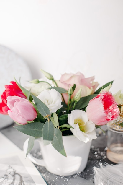Bouquet primaverile in vaso bianco su supporto in legno bianco. Rose, tulipani e lisianthus.
