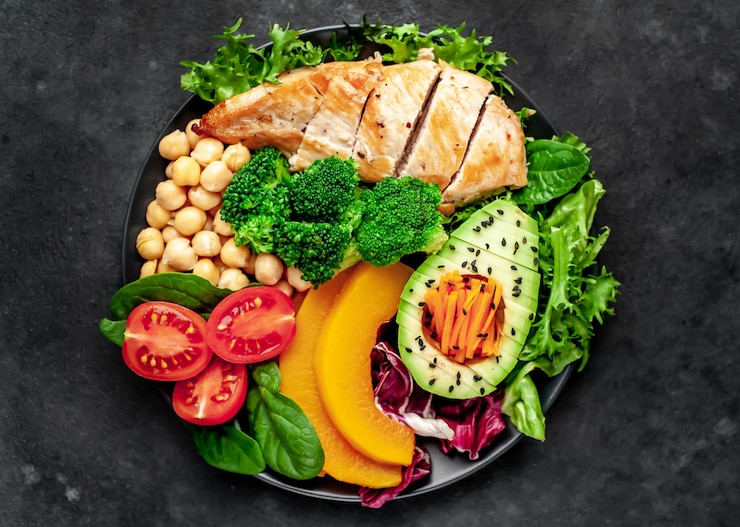 Foto bowl buddha. pollo, broccoli, ceci, zucca, avocado, carota, pomodoro, lattuga su un piatto con coltello e forchetta