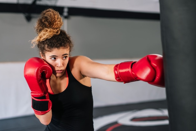 Boxer donna formazione con guantoni da boxe rossi punzonatura direttamente in un sacco da boxe in una palestra