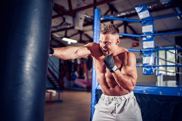 Boxer maschio formazione con sacco da boxe nel buio palazzetto dello sport. Giovane pugile formazione sul sacco da boxe.
