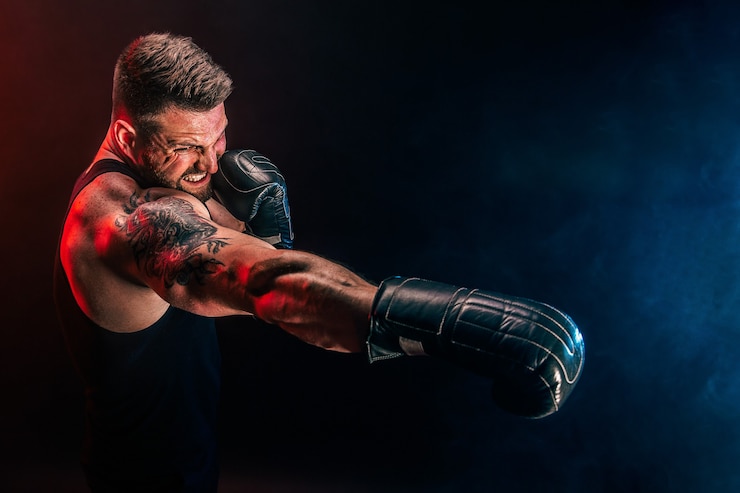 Foto boxer muay thai sportivo tatuato barbuto in canottiera nera e guantoni da boxe combattendo sul muro scuro con fumo. concetto di sport.