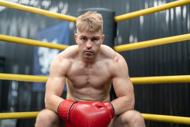 Boxer uomo seduto in un angolo sul ring di boxe in palestra Boxer maschio di MMA in cerca di un concorrente tra i round