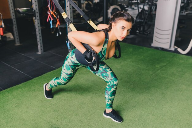 braccia allenamento donna con cinghie di fitness trx in palestra facendo flessioni treno parte superiore del petto spalle tricipiti pettorali.