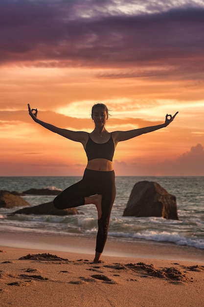 Braccia di posizione yoga della donna sollevate sulla costa del mare tropicale o sulla spiaggia dell'oceano all'aperto al tramonto