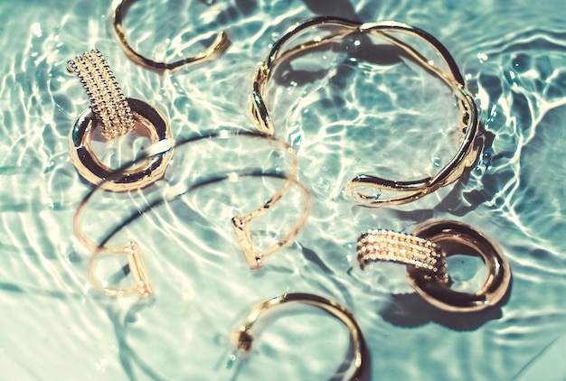 Braccialetti d'oro orecchini anelli gioielli su sfondo di acqua color smeraldo glamour di lusso e design di bellezza per le vacanze per annunci di marchi di gioielli