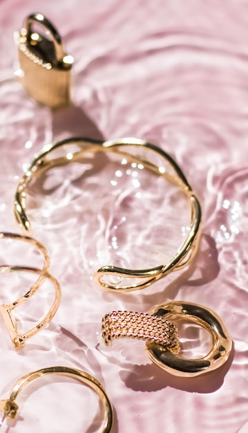 Braccialetti d'oro orecchini anelli gioielli su sfondo rosa acqua glamour di lusso e design di bellezza per le vacanze per annunci di marchi di gioielli