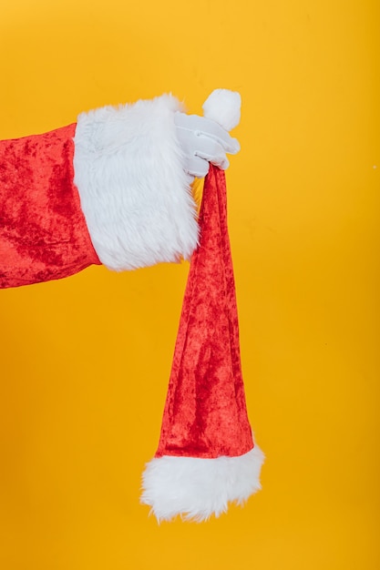 Braccio di Babbo Natale che tiene un suo cappello su giallo