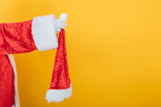 Braccio di Babbo Natale che tiene un suo cappello su giallo